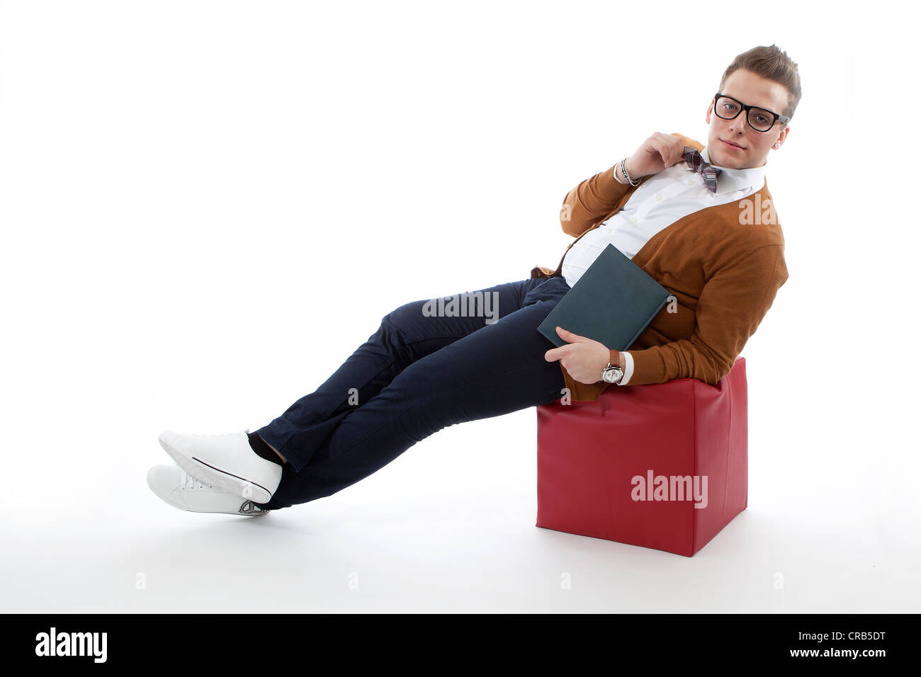 Jeune homme avec des lunettes et un chapeau assis sur un cube Banque D'Images