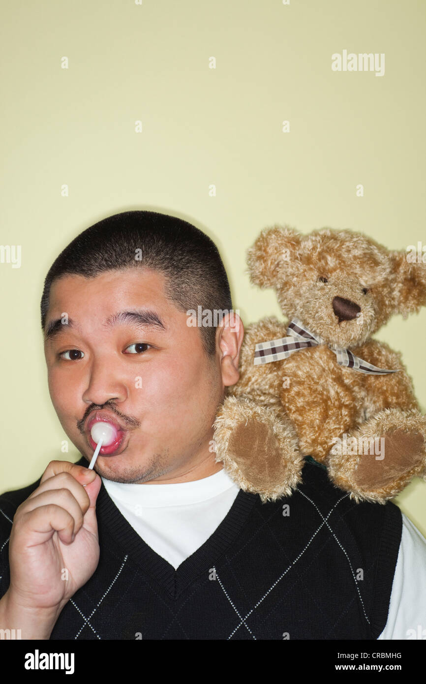 Portrait d'un homme enfantin de sucer une sucette, ours en peluche sur l'épaule Banque D'Images