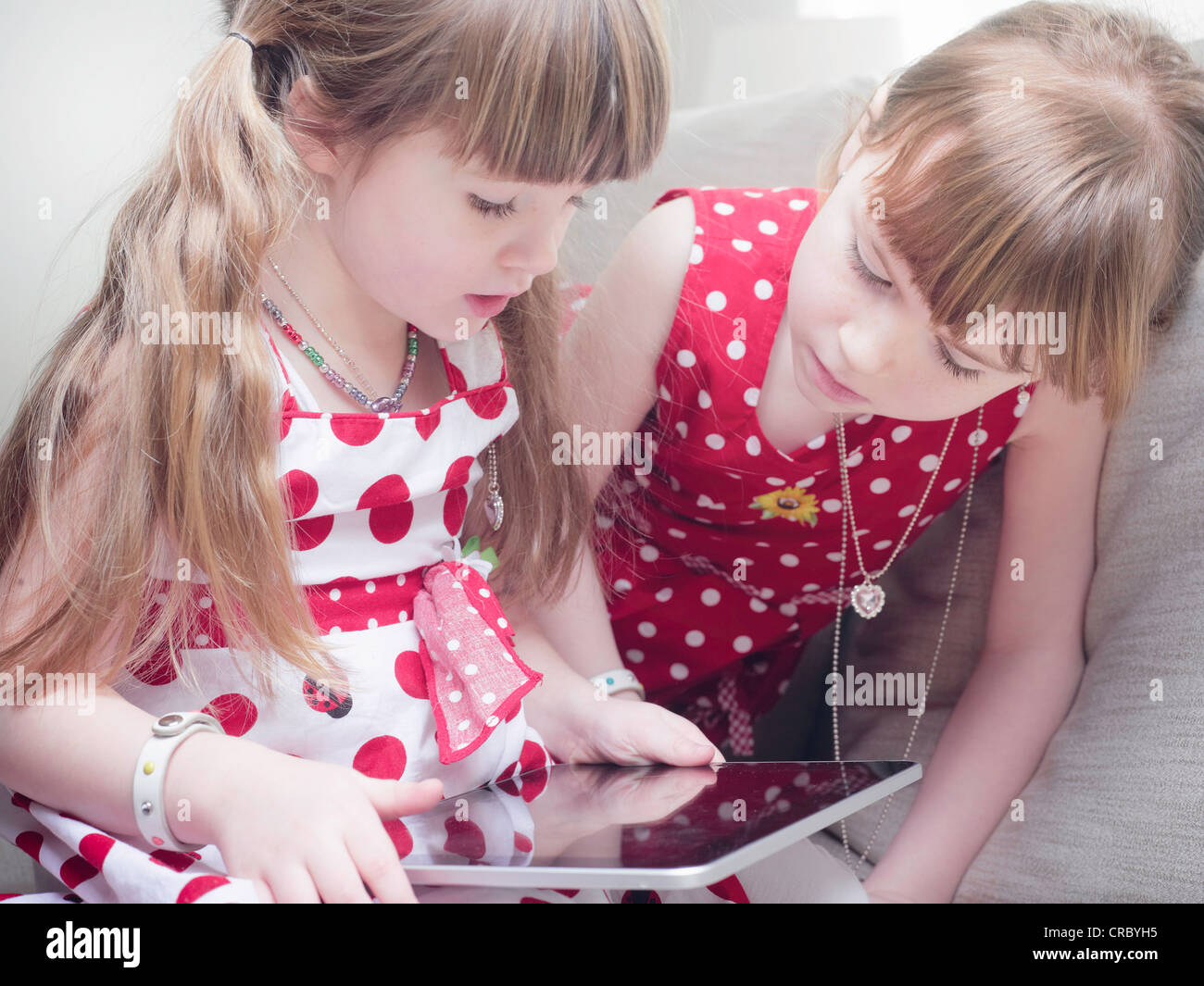 Girls using tablet computer on sofa Banque D'Images