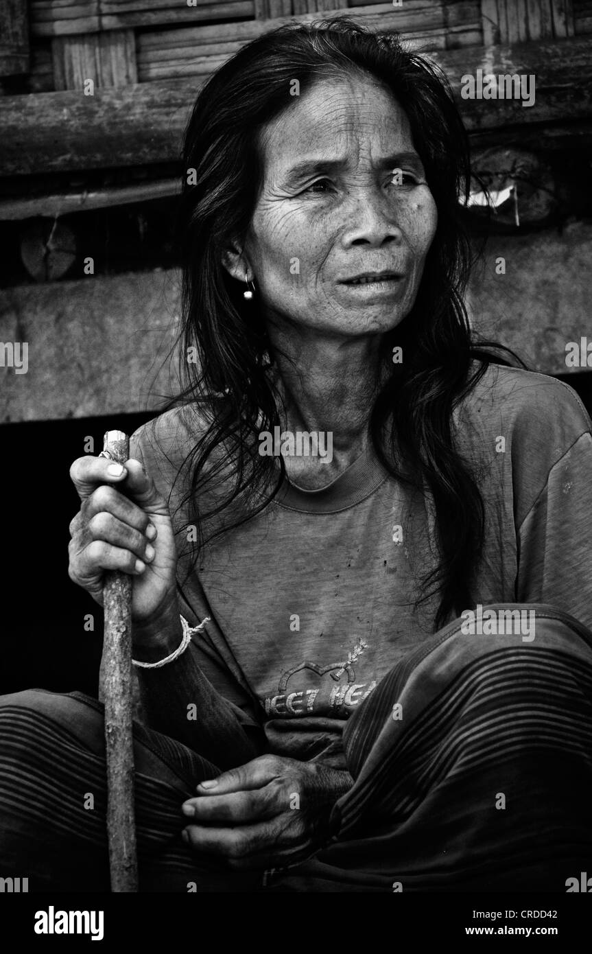 Vieille Femme avec un bâton assis devant une cabane en bambou, dans un village sur la rivière du Mékong, Laos, Asie du Sud, Asie Banque D'Images