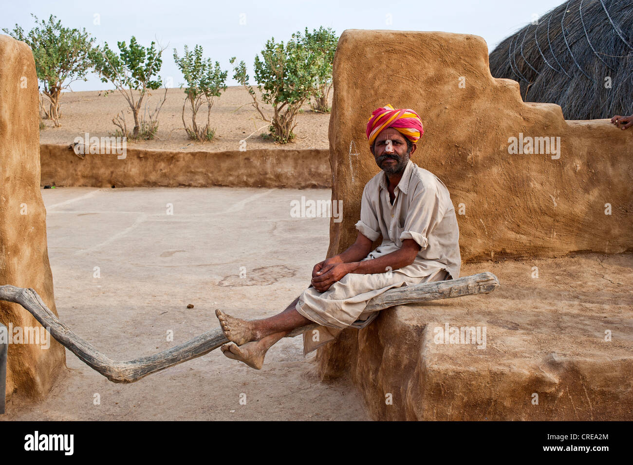L'homme indien, vêtu d'un dhoti et d'une tiare, assis en face de sa porte de la cour avec ses jambes nonchalamment placé sur un bâton en bois Banque D'Images
