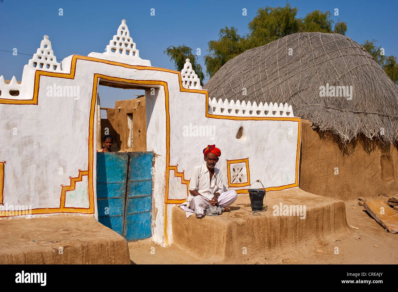 Rajasthani, indien vêtu d'un dhoti et turban, assis en face de son traditionnellement construit et peint porte avant Banque D'Images