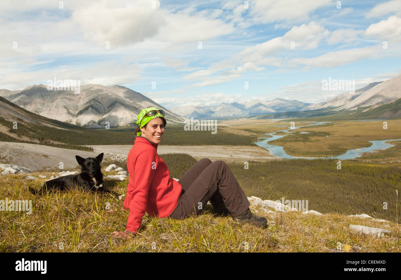 Jeune femme assise, se reposer, profiter de la vue, panorama, Alaskan Husky, chien de traîneau à côté d'elle, Wind River valley et Mackenzie Banque D'Images