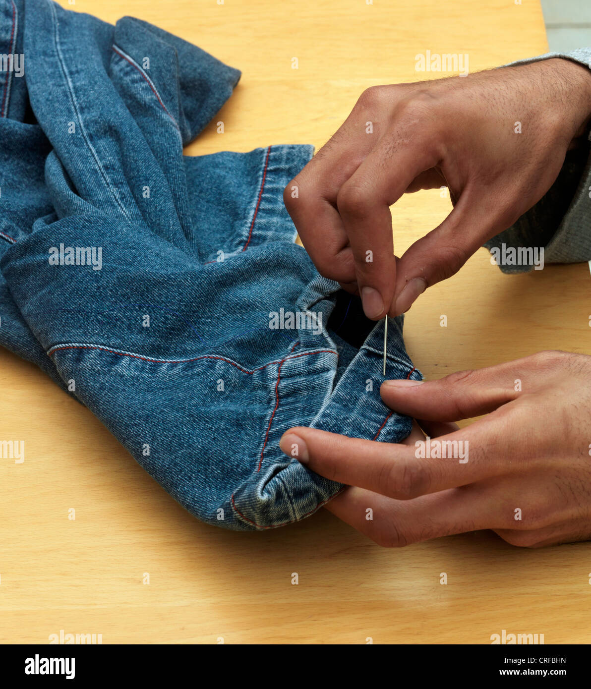 Les mains de l'homme afro-antillaise ourlet à coudre sur Denim Jeans avec aiguille et fil Banque D'Images