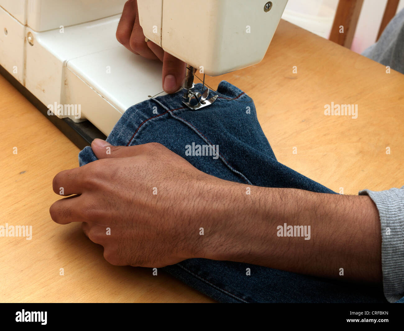 Les mains de l'homme afro-antillaise sur l'ourlet à coudre Machine à coudre à l'aide de Jeans Banque D'Images