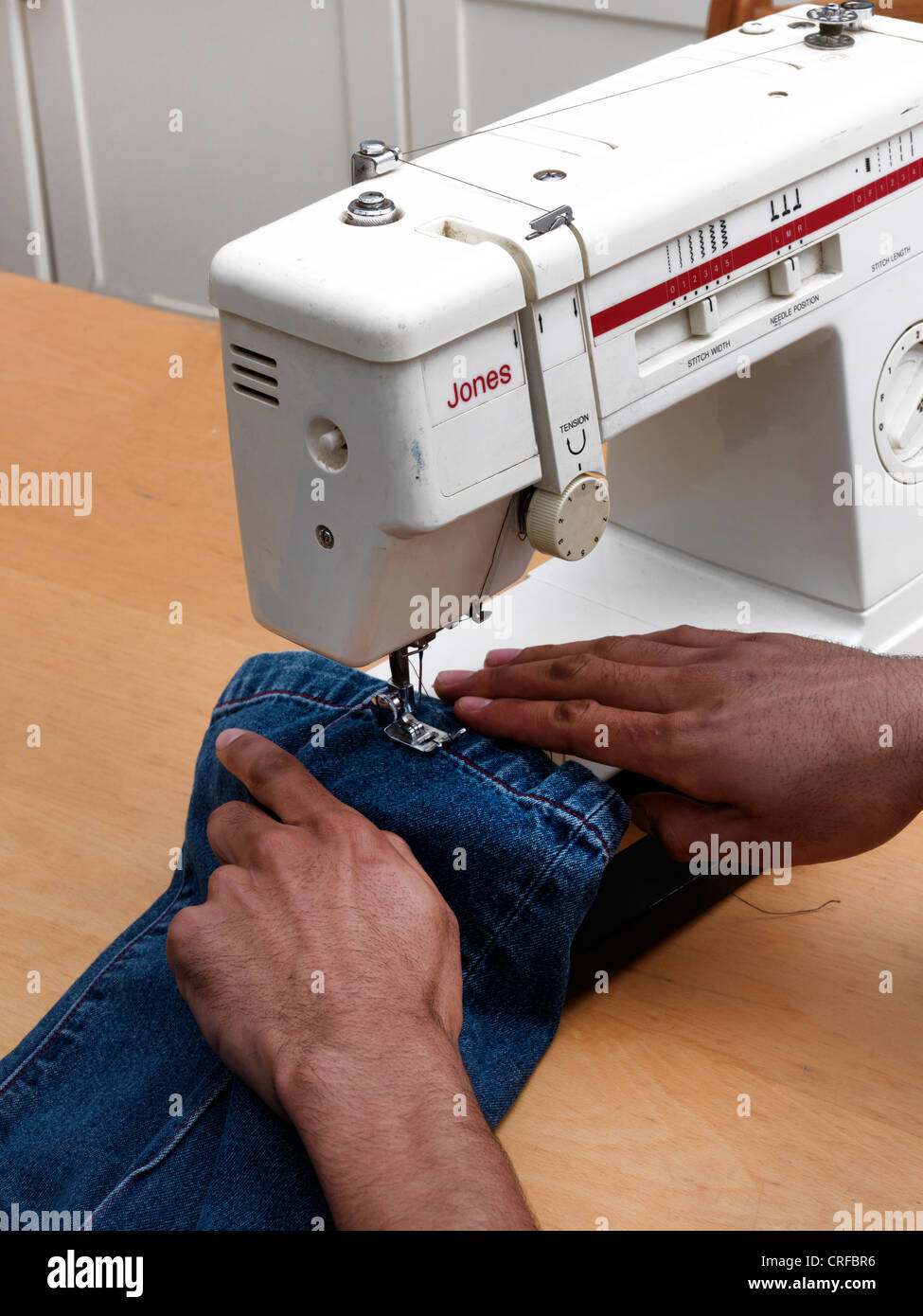 Les mains de l'homme afro-antillaise sur l'ourlet à coudre Machine à coudre à l'aide de Jeans Banque D'Images