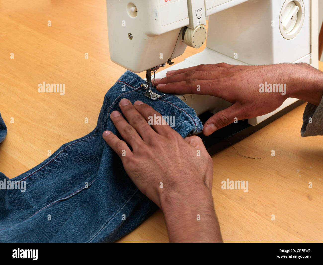 Les mains de l'homme afro-antillaise sur l'ourlet à coudre Machine à coudre à l'aide de Jeans Banque D'Images