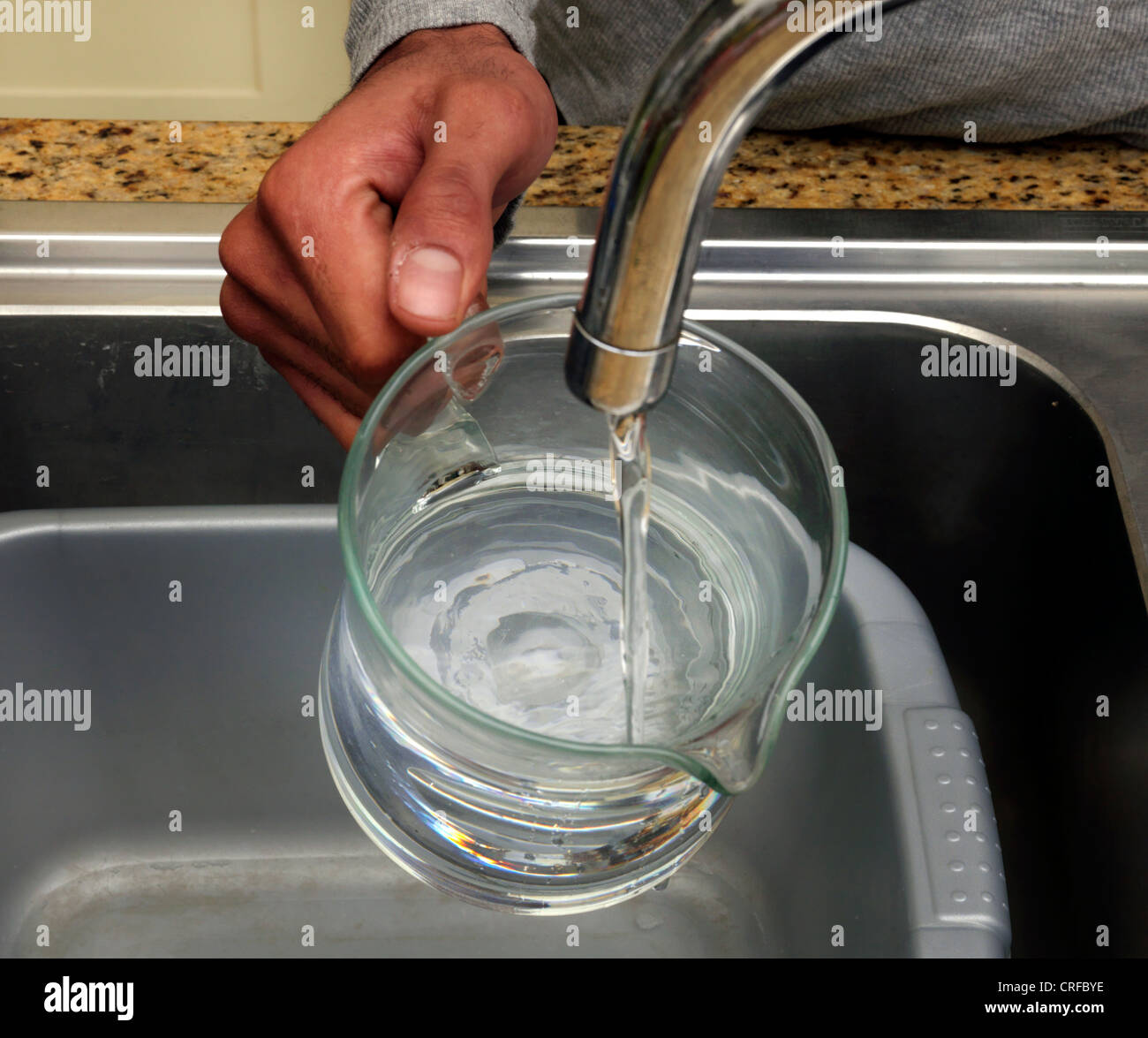 Les mains de l'homme afro-antillaise d'eau de remplissage dans une cruche en verre à partir d'un robinet Banque D'Images