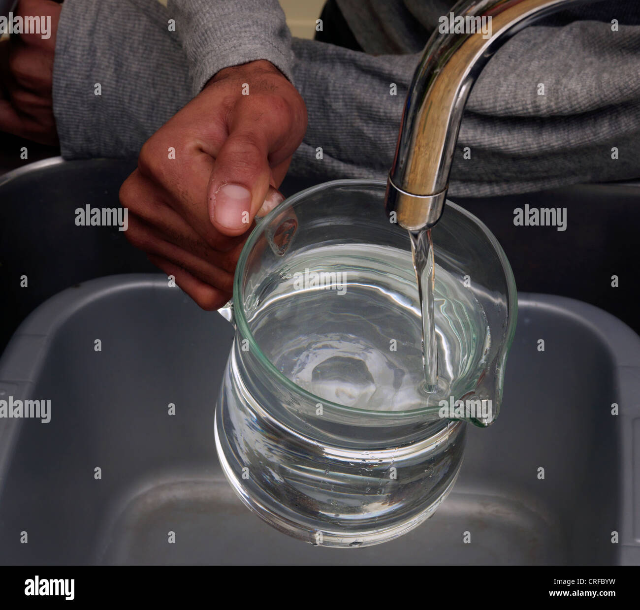 Les mains de l'homme afro-antillaise d'eau de remplissage dans une cruche en verre à partir d'un robinet Banque D'Images