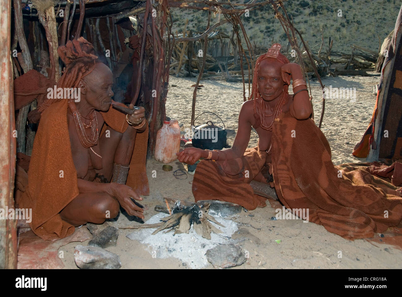 Village traditionnel de Purros femmes Himba, fumeurs en face d'une hutte, Namibie, Purros Banque D'Images