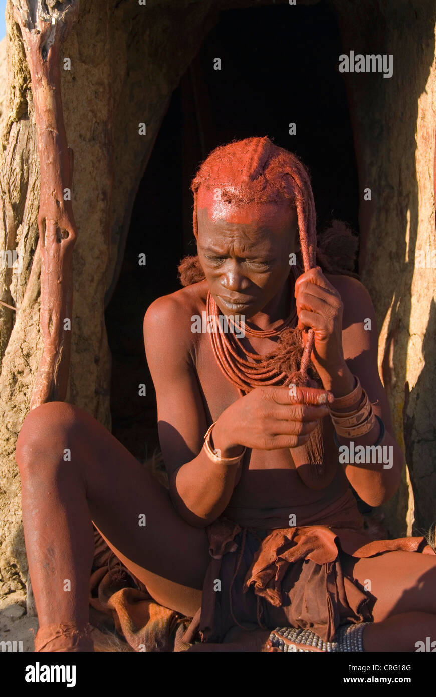 Village traditionnel de Purros, femme Himba habiller ses cheveux dans la matinée, la Namibie, Purros Banque D'Images