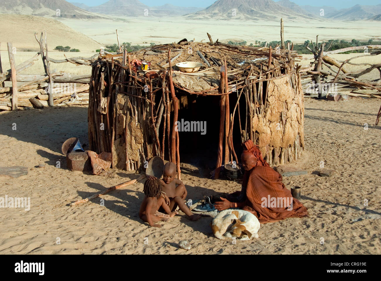 Village traditionnel de Purros, femme Himba avec les enfants et le chien en face d'une hutte, Namibie, Purros Banque D'Images