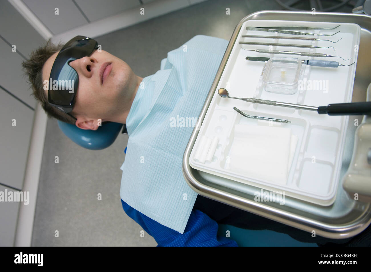 Young male patient dans le fauteuil du dentiste en face d'un plateau d'instruments dentaires Banque D'Images