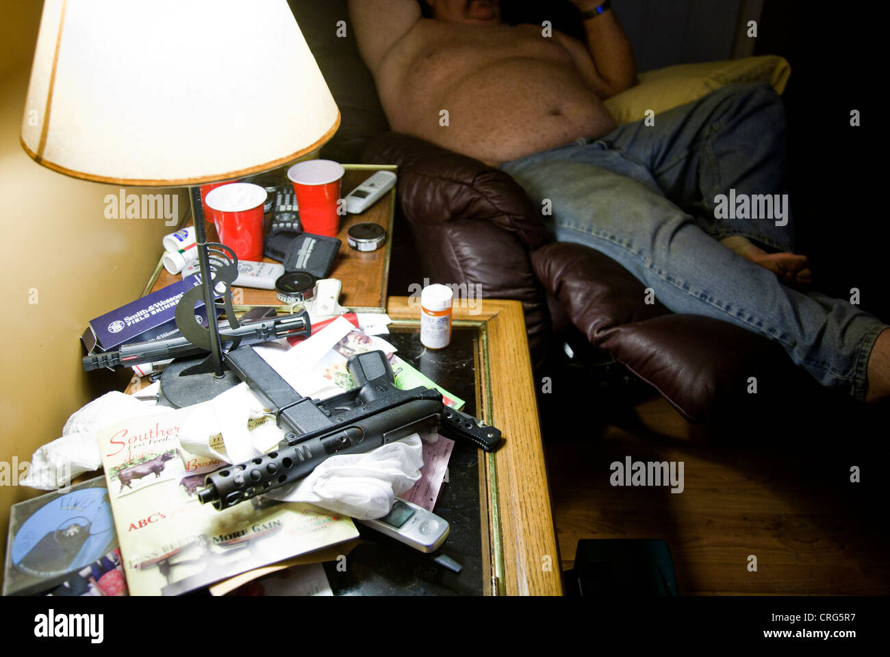Un pistolet automatique et deux pistolets, s'asseoir sur une table avec une lampe dans un salon de l'homme. L'homme est assis sur une chaise en arrière-plan le port de Banque D'Images