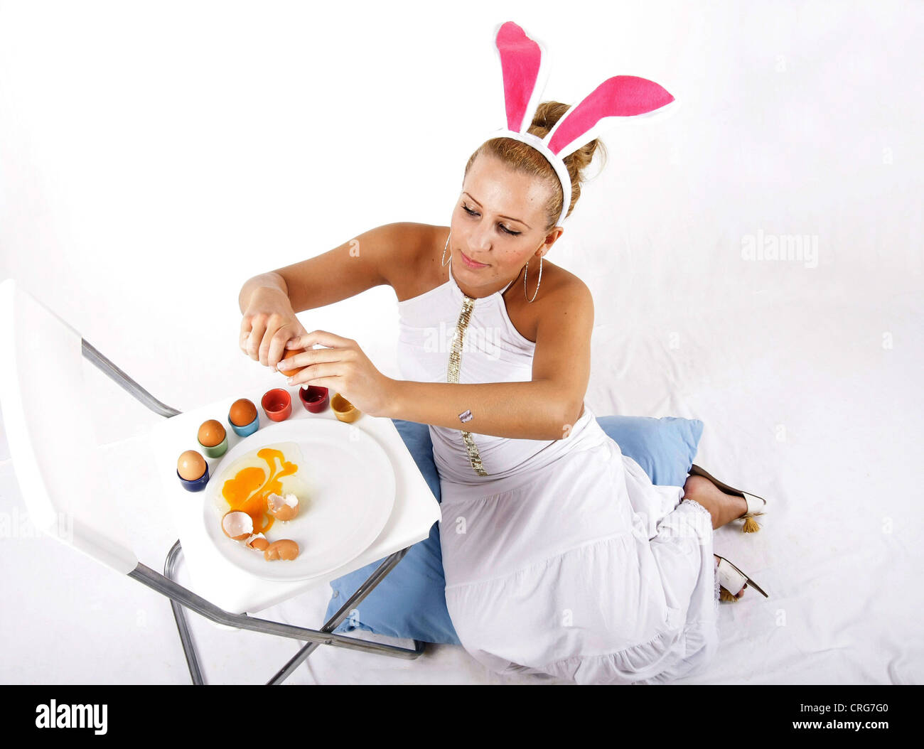 Jeune femme avec des oreilles de lapin rose ouvre les œufs, en versant le jaune d'un oeuf Banque D'Images