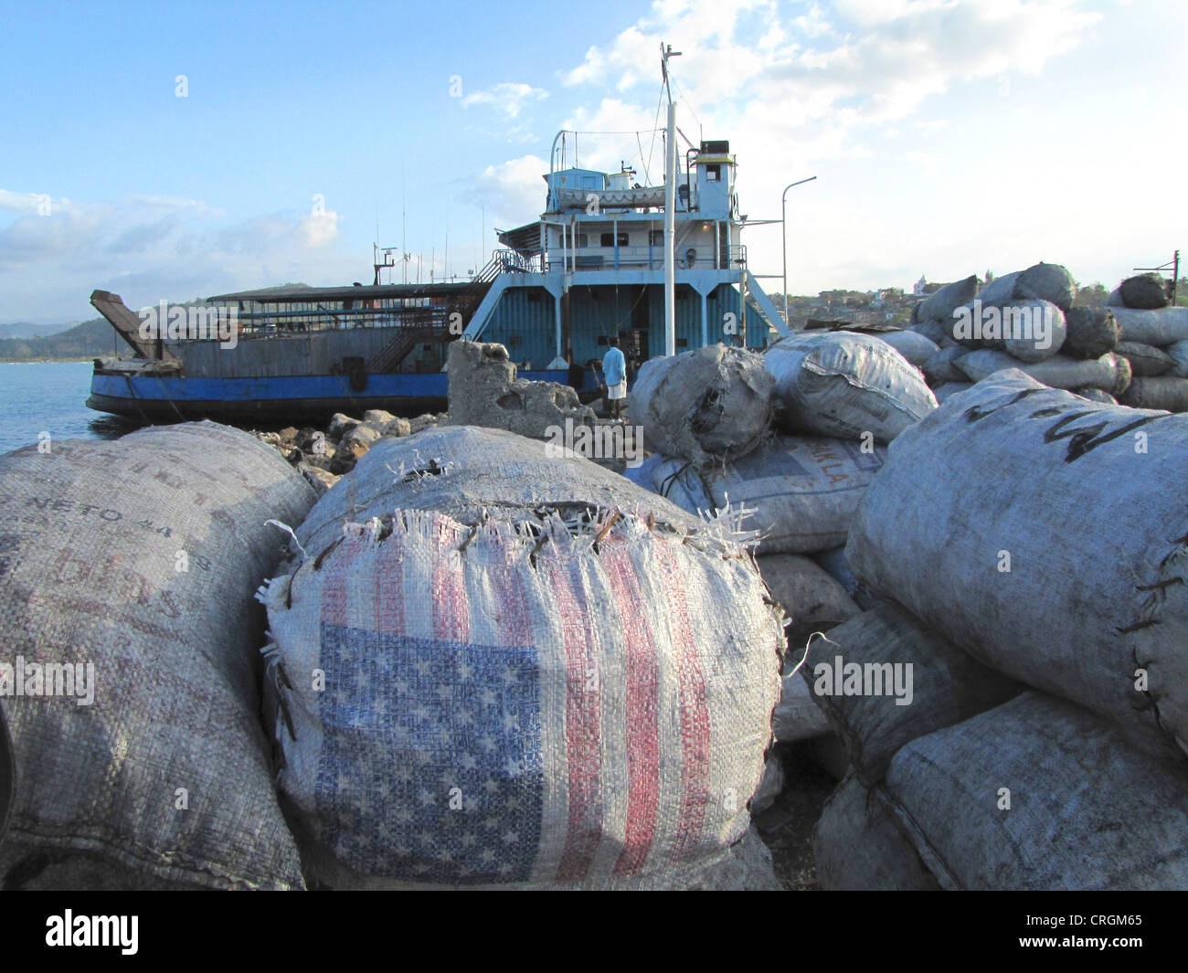 Sacs empilés, certaines avec nous drapeau sur eux, dans le port de Jrmie, ferry en arrière-plan, Haïti, Grande Anse, Jeremie Banque D'Images