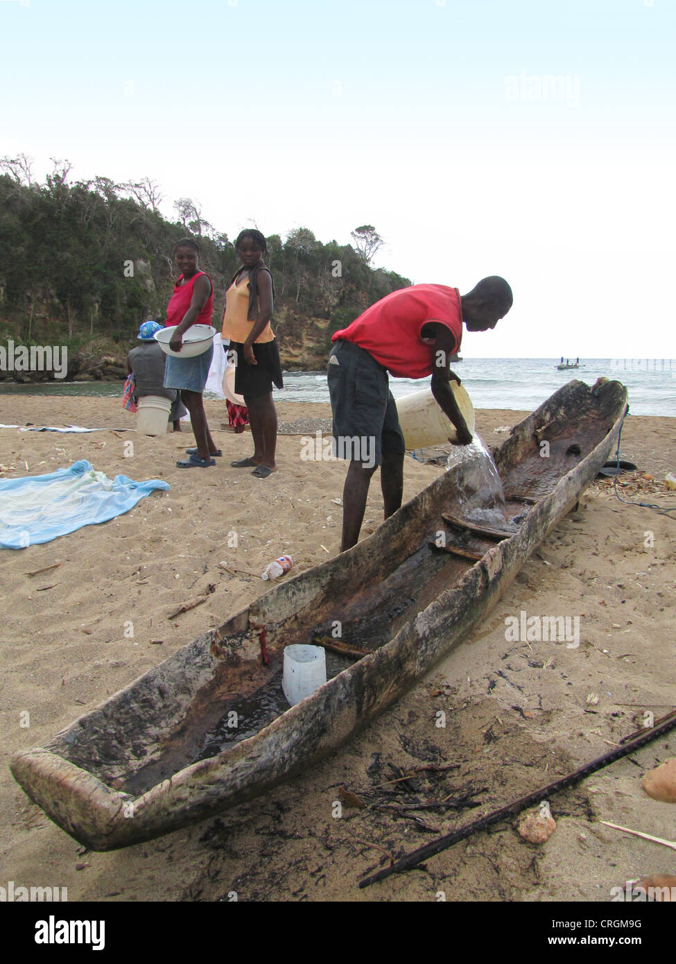 Nettoyage du bateau de son homme fait d'un mango-évidé, arbres en arrière-plan de la mer des Caraïbes, Haïti, Grande Anse, Abricots Banque D'Images