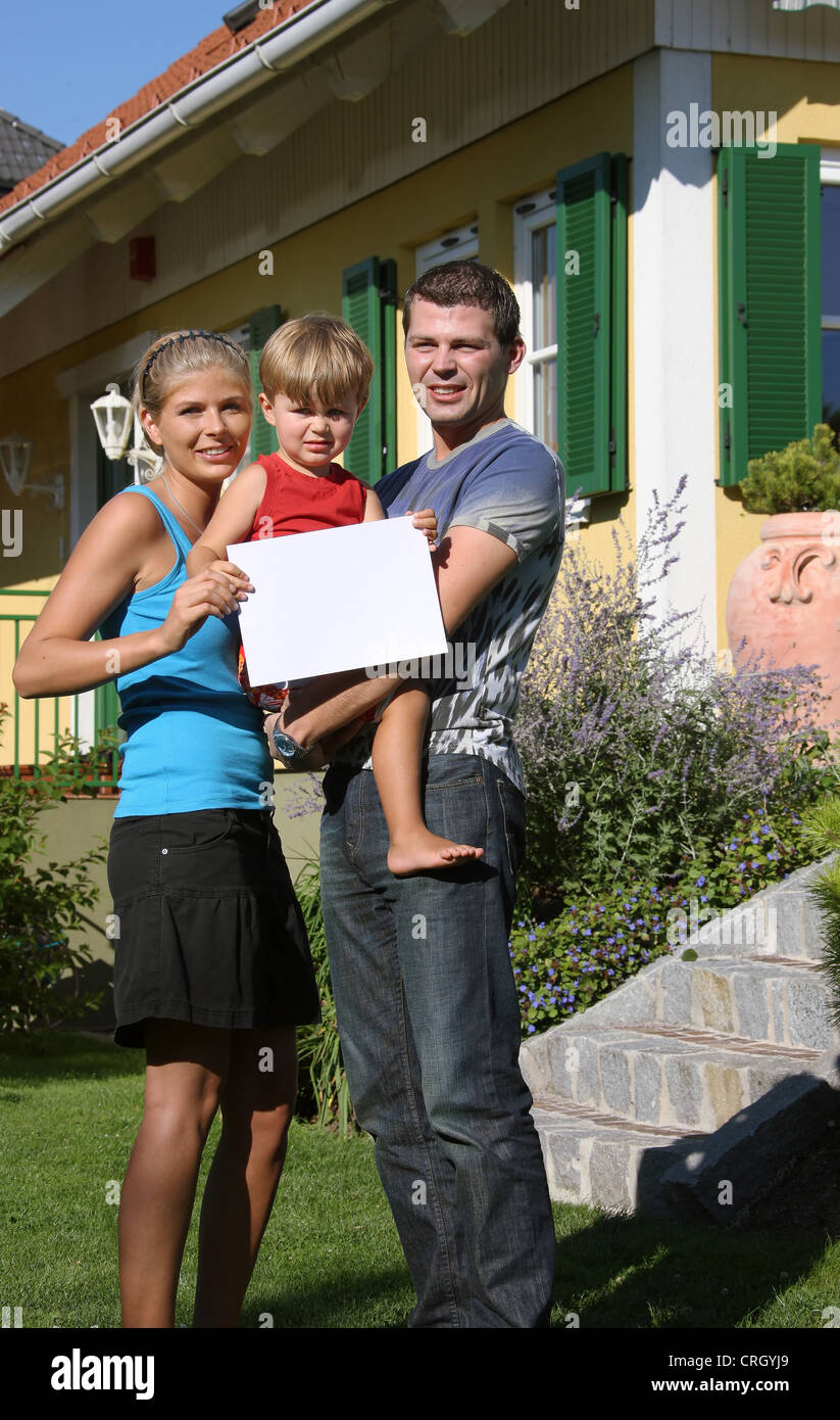 Jeune famille debout avec un blank sign devant leur nouvelle maison Banque D'Images