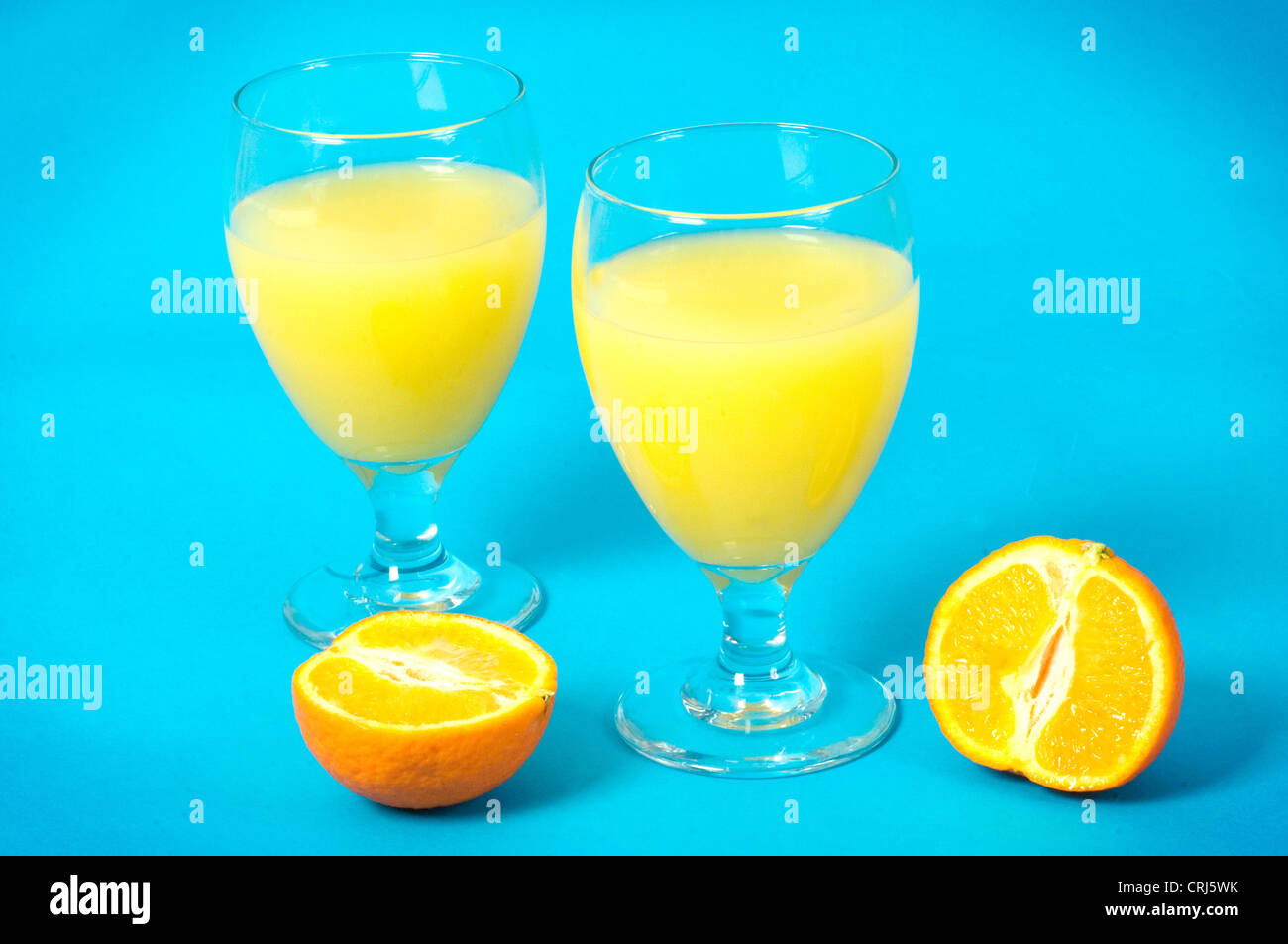 Verres de jus d'orange et oranges sur un fond bleu. L'orange est une excellente source de vitamine C (acide ascorbique) et de potassium, ce qui peut aider à lutter contre le rhume et peut également aider à protéger votre cœur contre les dommages. C'est aussi une importante source naturelle d'acide folique (B9) qui est recommandée pour les femmes qui sont enceintes. Une carence en vi Banque D'Images
