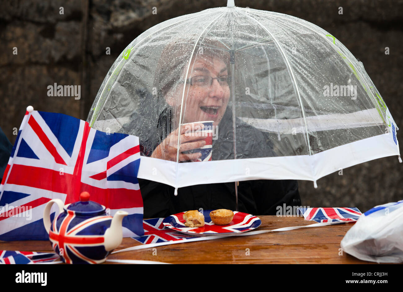 Les refuges d'une femme de la pluie au cours d'une partie de la rue de la célébrations du Jubilé de diamant de la Reine à Morecambe, UK. Banque D'Images