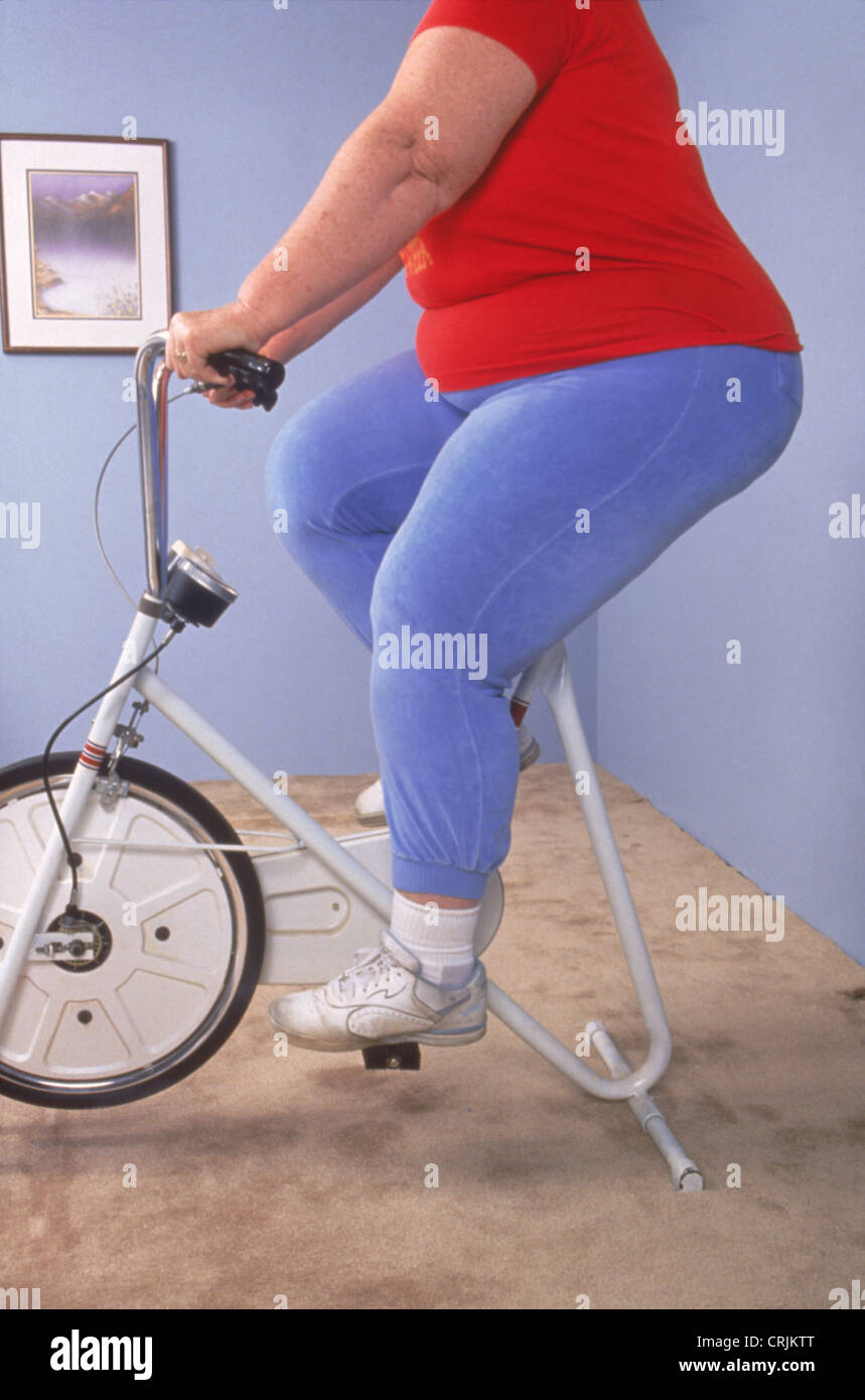 Femme obèse sur le vélo à la maison de la machine Banque D'Images