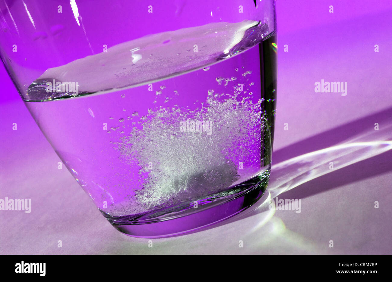 Un comprimé effervescent se dissout dans un verre d'eau contre un fond violet. Banque D'Images