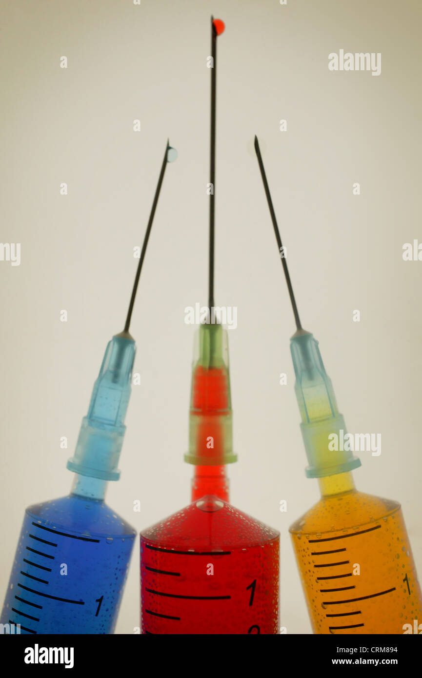 Trois seringues hypodermiques jetables contenant des liquides de différentes couleurs. Banque D'Images