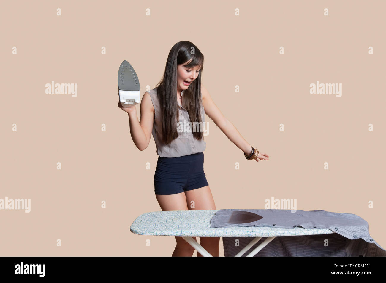 Choqué woman chemise brûlée sur une planche à repasser sur fond coloré Banque D'Images