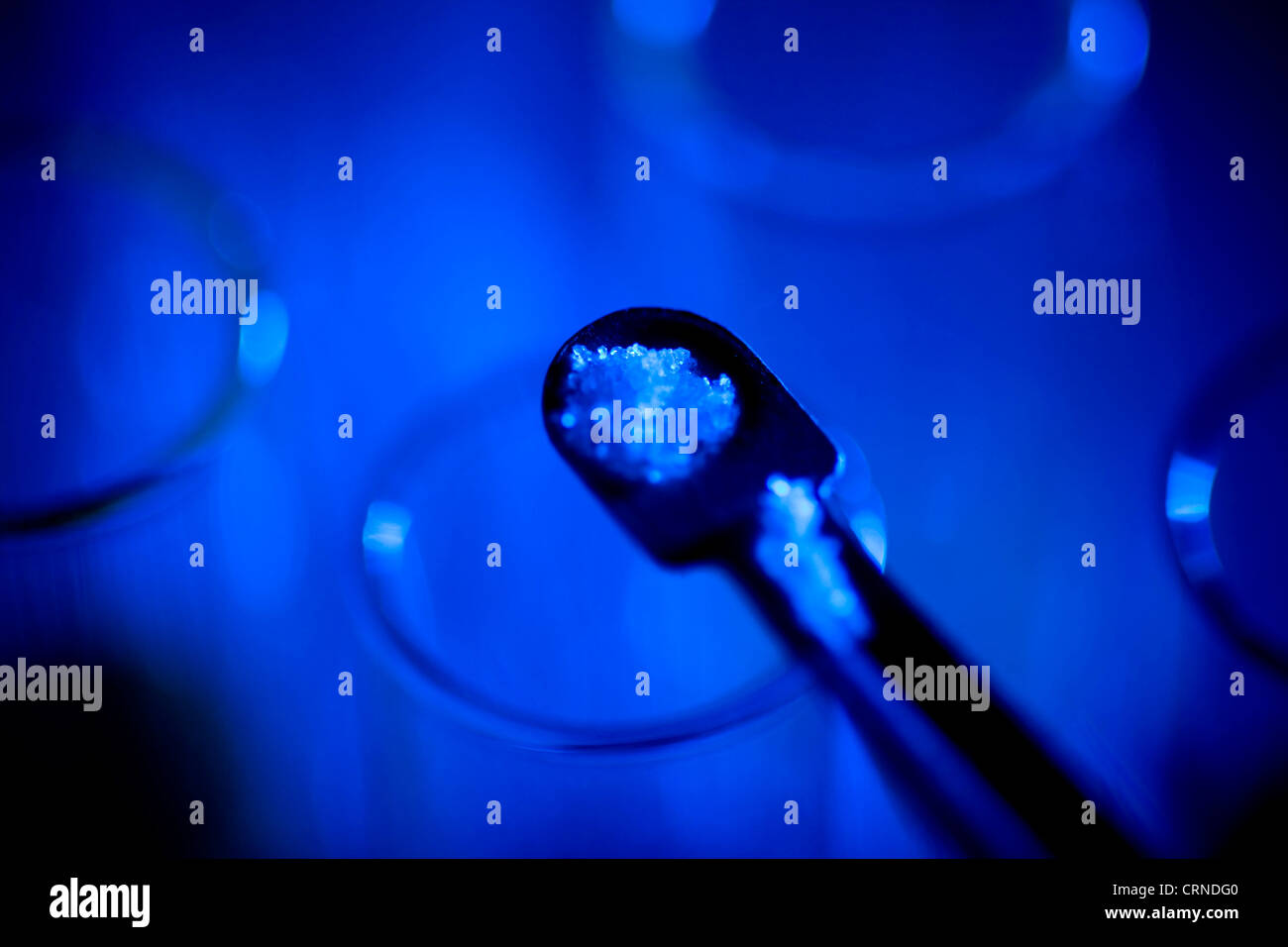 Une spatule de chlorure de sodium (sel de mer) est versé dans un tube à essai sur un fond bleu. Banque D'Images
