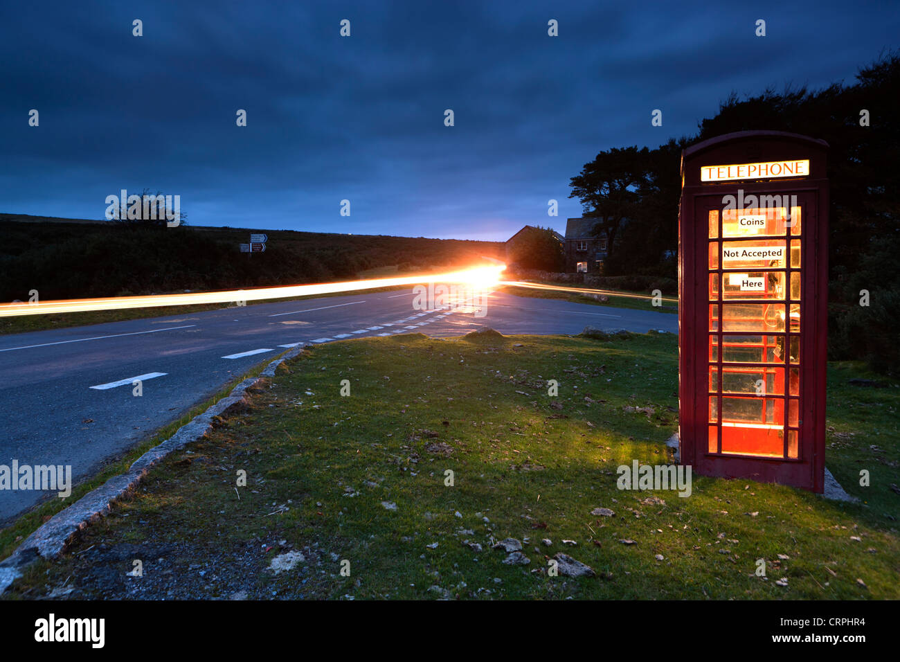 Sentier de lumière à partir d'une voiture passe une boîte de téléphone rouge par le côté d'une route dans le parc national du Dartmoor. Banque D'Images