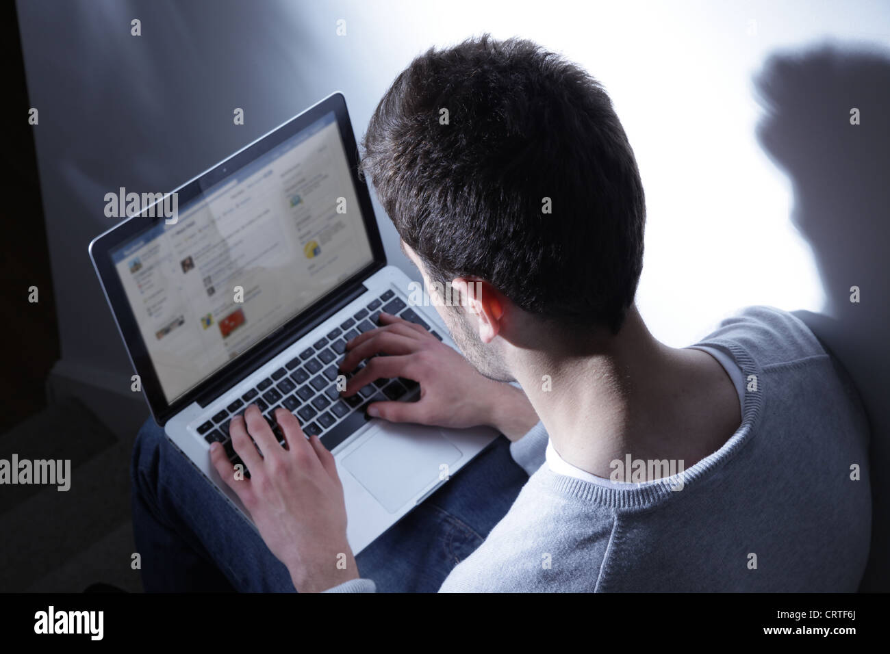 Jeune homme assis dans le noir avec son ordinateur portable, Ttweeting. Banque D'Images