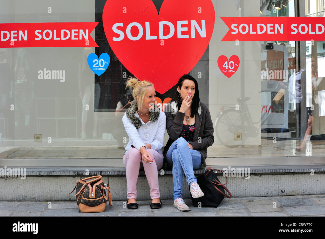 Deux filles et commode les panneaux signalant les déductions dans la fenêtre vide shop de sold out store au cours de l'été shopping ventes Banque D'Images