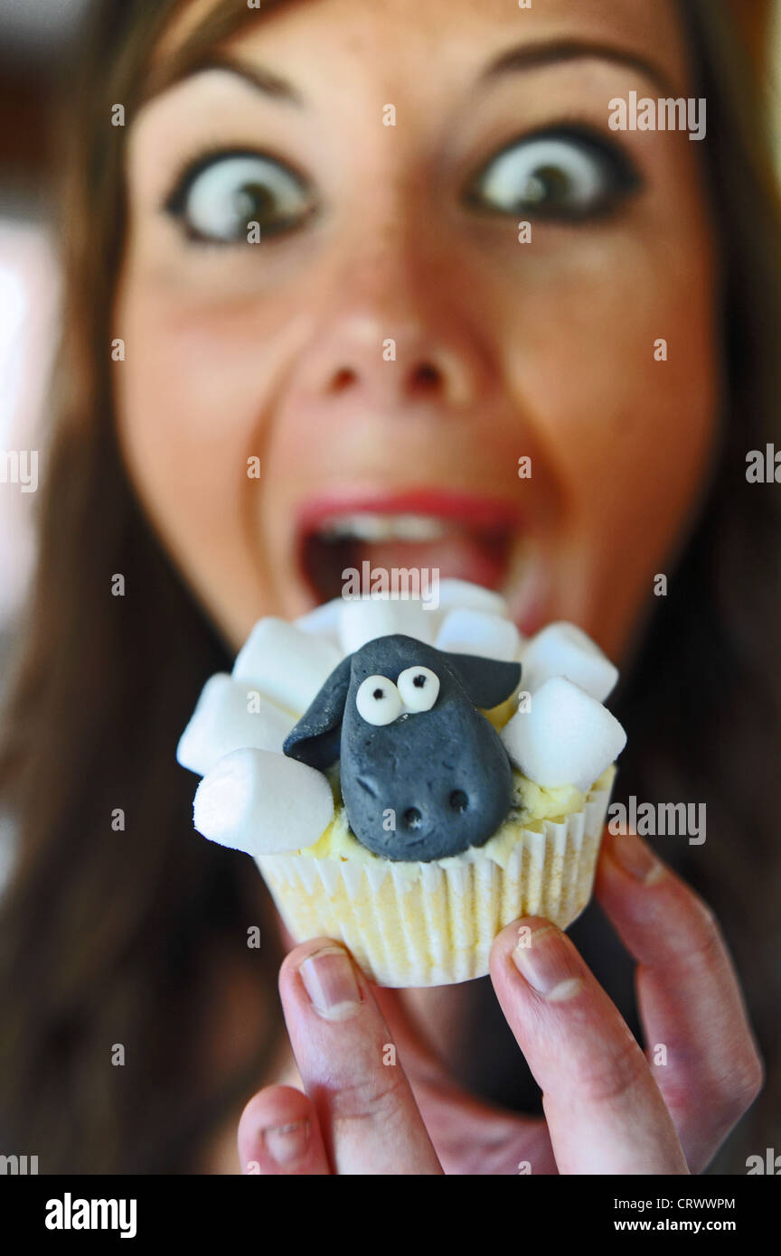 Cupcake fait maison dans la conception de l'enfant caractère Aardman tv Shaun le mouton sur le point d'être mordu par jeune femme Banque D'Images