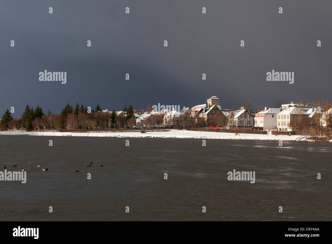 Maisons et bâtiments bordant l'étang, Reykjavik, Islande, sous un ciel gris orageux Banque D'Images