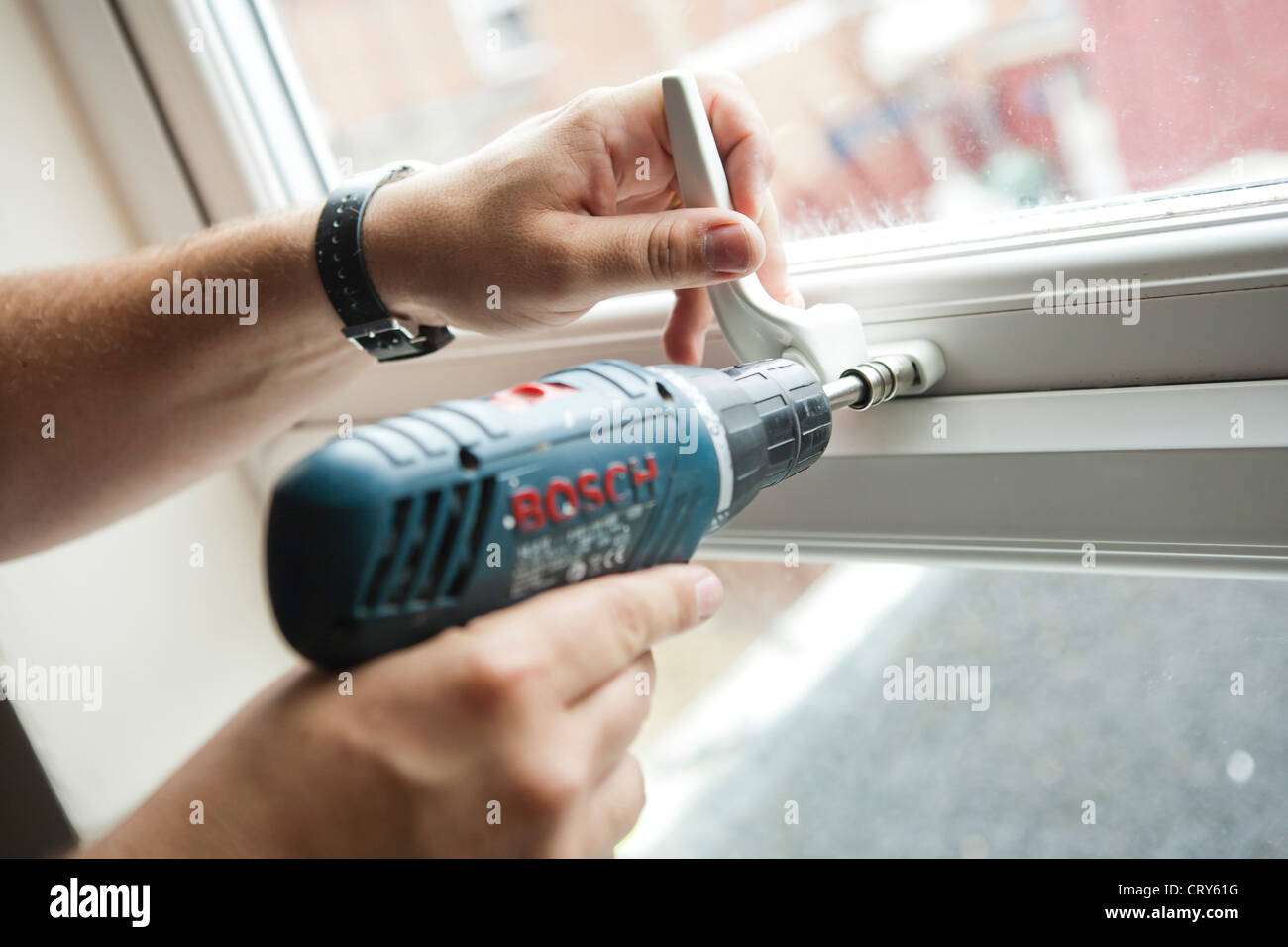 Un ouvrier utilise une perceuse Bosch GSR14. pour visser un écrou de blocage sur la poignée d'une fenêtre Banque D'Images