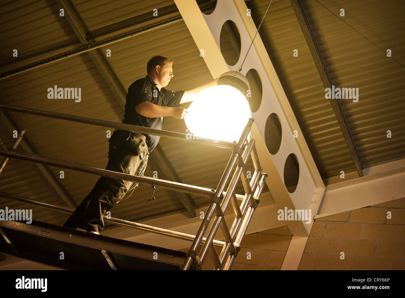 Changements Workman lampe à vapeurs de sodium ampoule en sports hall roof sur des échafaudages Banque D'Images