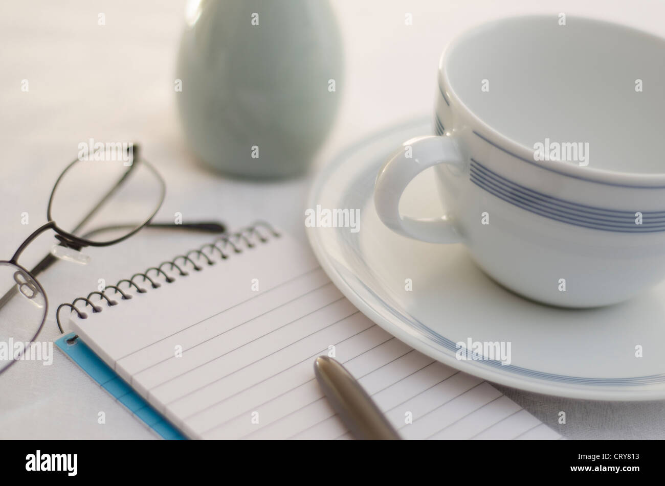 Table de coupe propre, lumineux avec scène de tasse de café, le bloc-notes et stylo, lunettes de lecture et de vase. Banque D'Images