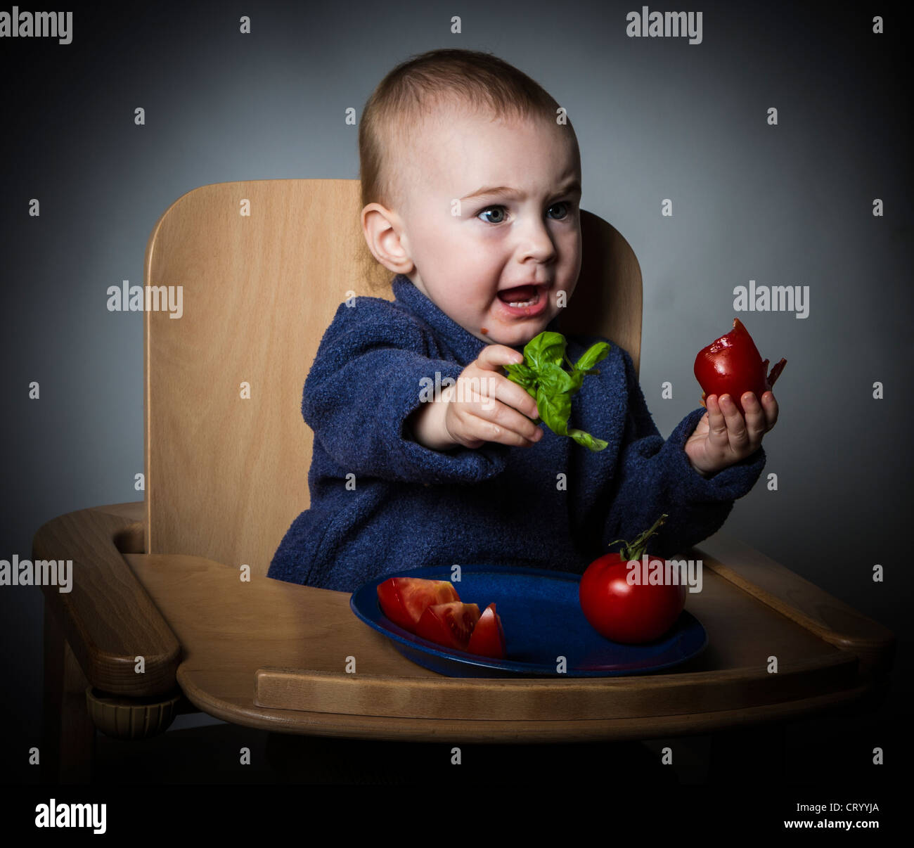 Jeune enfant de manger les tomates dans une chaise haute. Fond sombre Banque D'Images