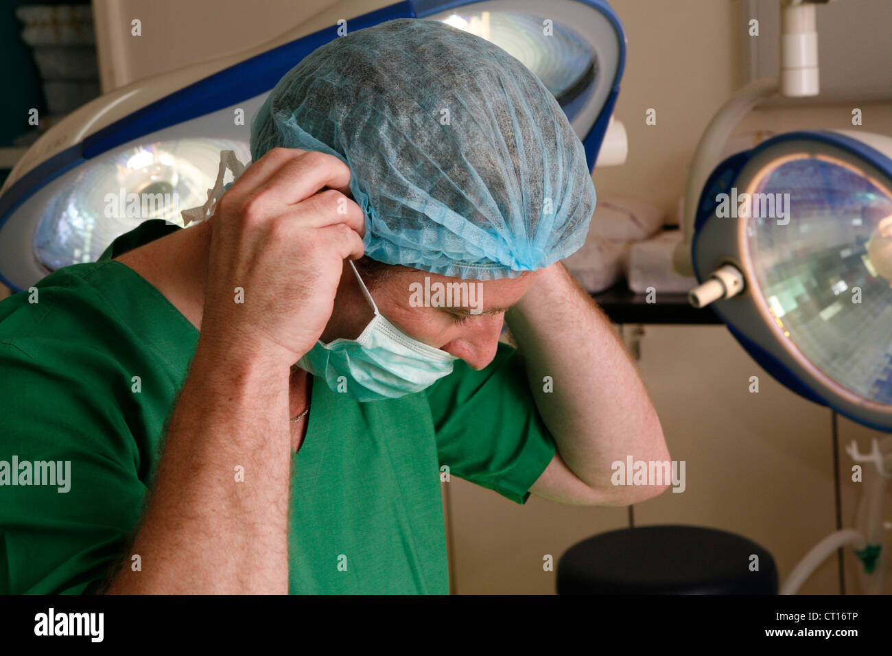 Un chirurgien de l'hôpital ajuster son masque chirurgical sous la lumière dans une salle d'opération. Banque D'Images