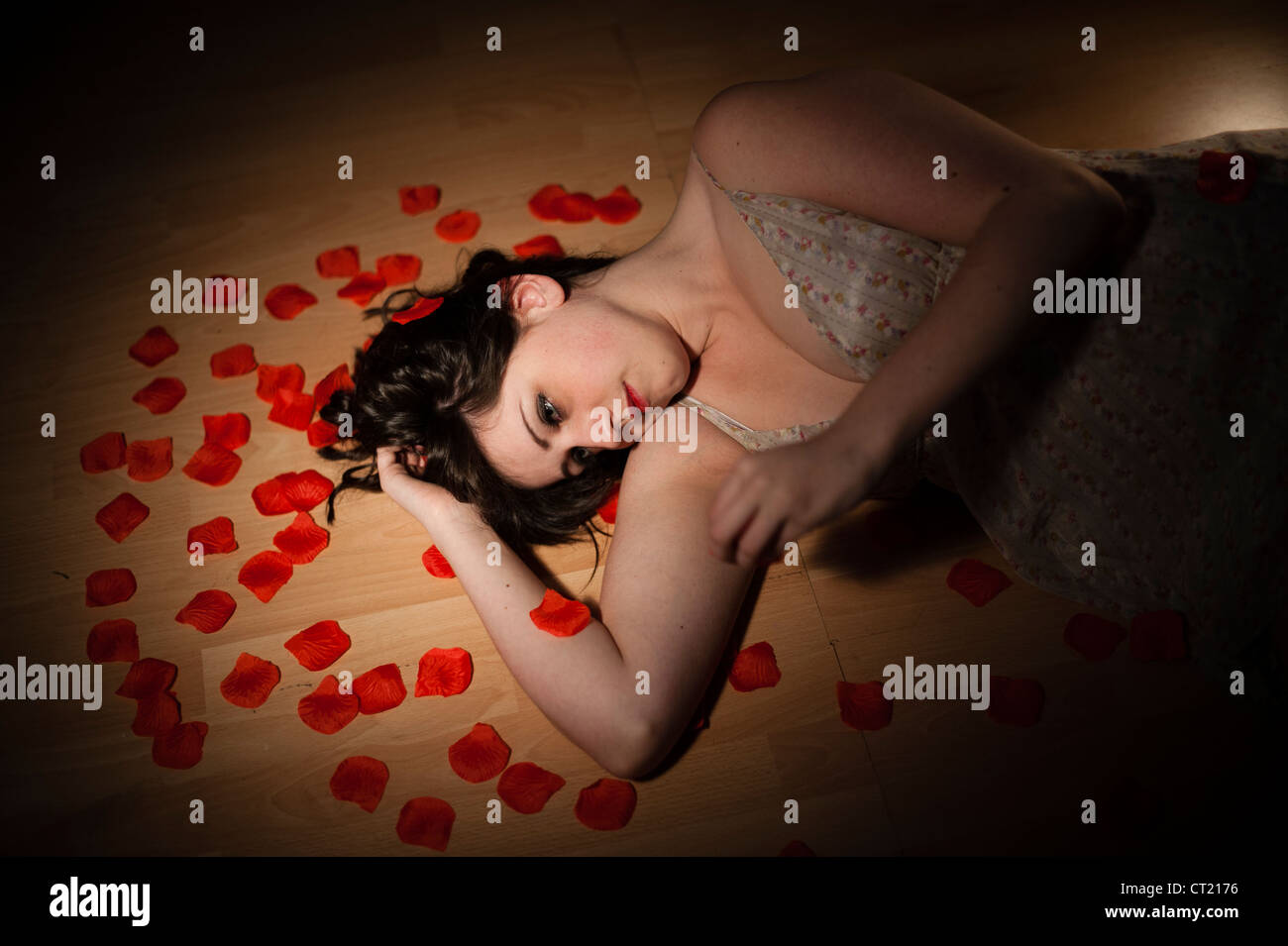 Une jeune femme fille seul couché sur la dispersion des pétales rouges sur un sol en bois Banque D'Images