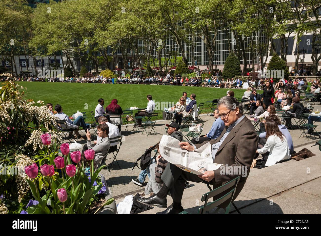 Homme mûr parmi des centaines appréciant Bryant Park, NYC Banque D'Images