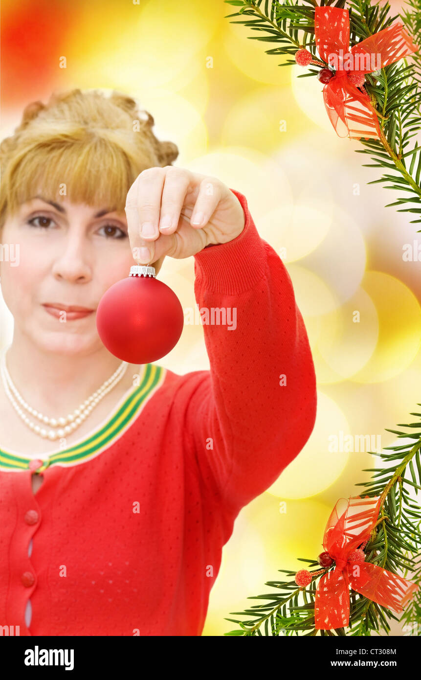 Célébration de Noël heureux avec smiling woman donnant une babiole rouge. Plus d'arbre de pin de fête et feux de la frontière de flou artistique. Banque D'Images
