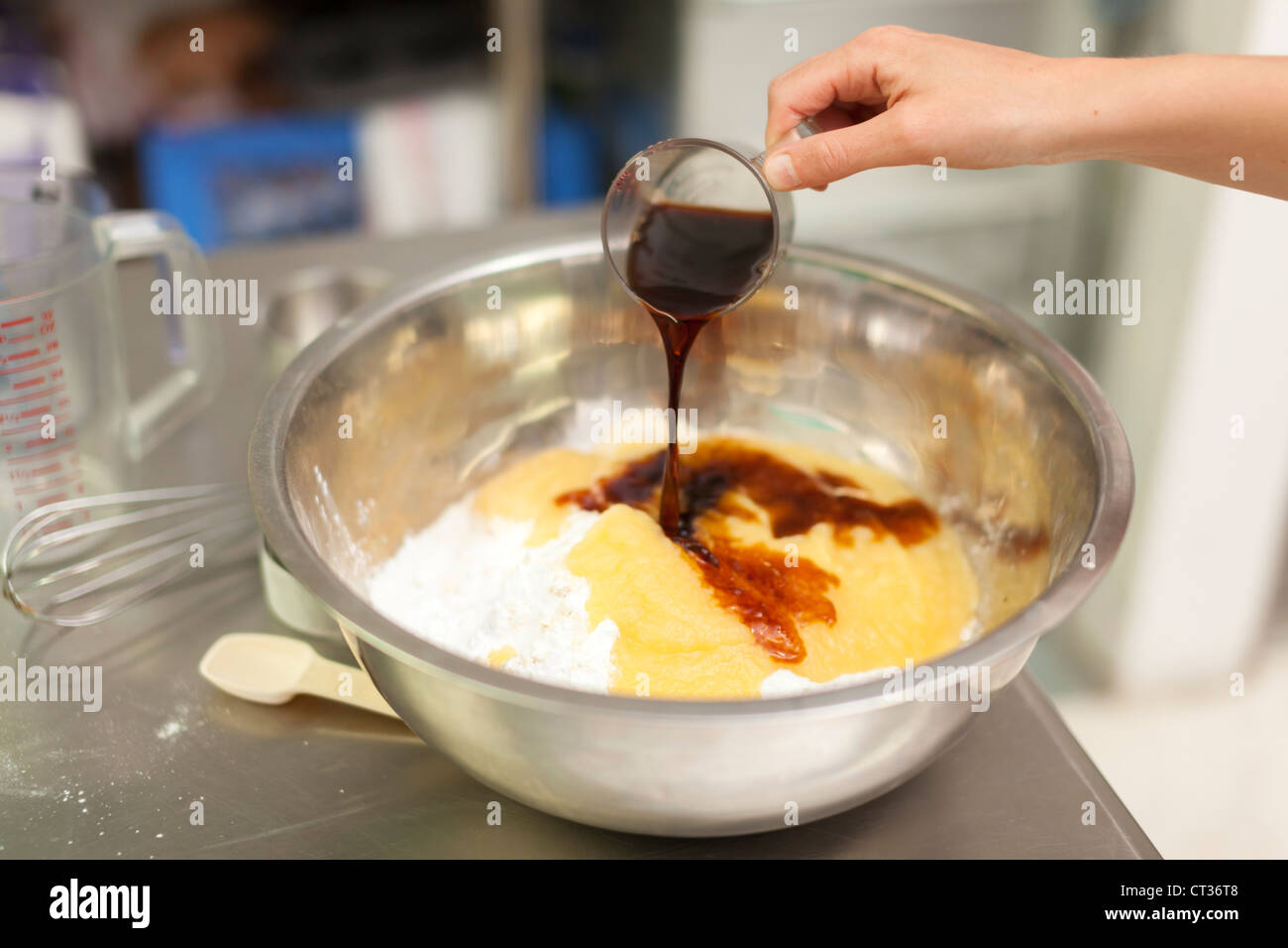 Une femme verse de l'extrait de vanille comme elle mélange des ingrédients dans un grand bol à mélanger pendant la cuisson des beignets à Tandmen Doughnu Banque D'Images