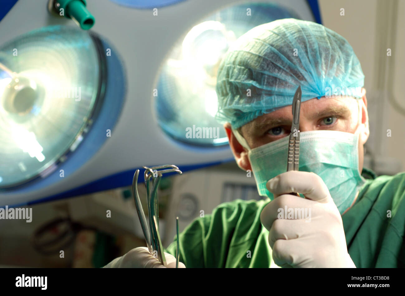 Un chirurgien masqué holding up un scalpel et une pince. Banque D'Images