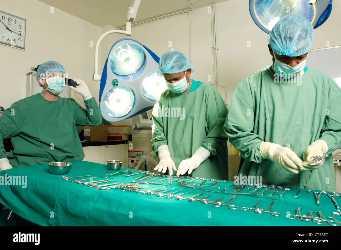 Le personnel du théâtre chirurgicale pose divers outils chirurgicaux sur la table d'opération alors que le chirurgien parle sur son téléphone mobile. Banque D'Images