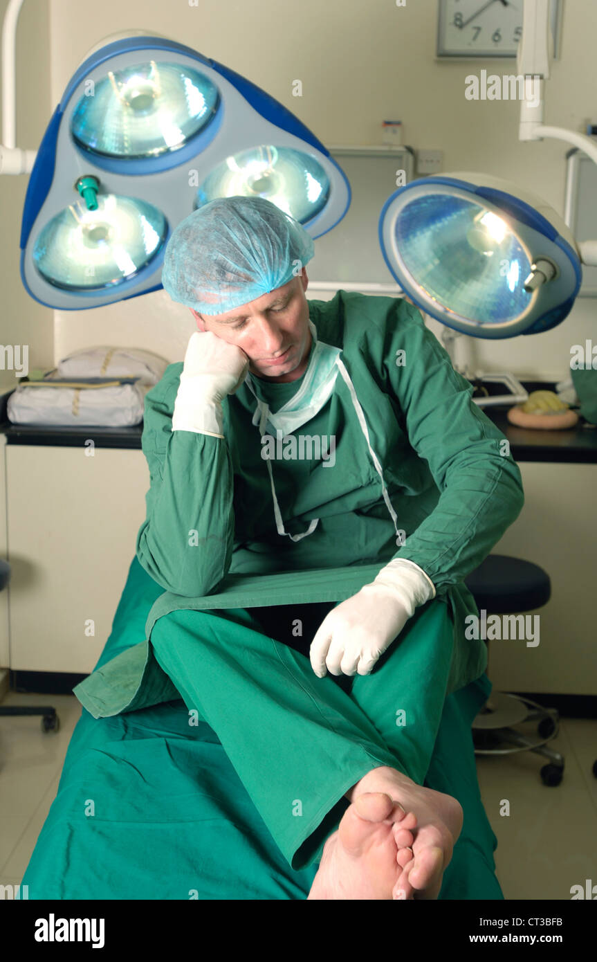Un chirurgien assis sur une table d'opération, se reposer ses yeux. Banque D'Images