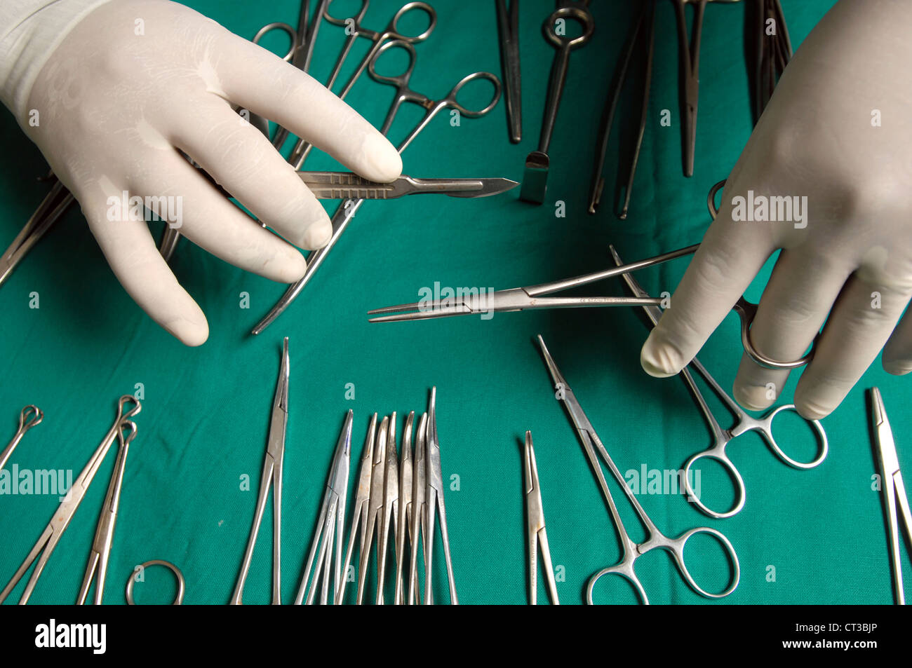 Gros plan sur les mains d'un chirurgien tenant un scalpel et une paire de pinces sur une table chargée de divers outils chirurgicaux. Banque D'Images