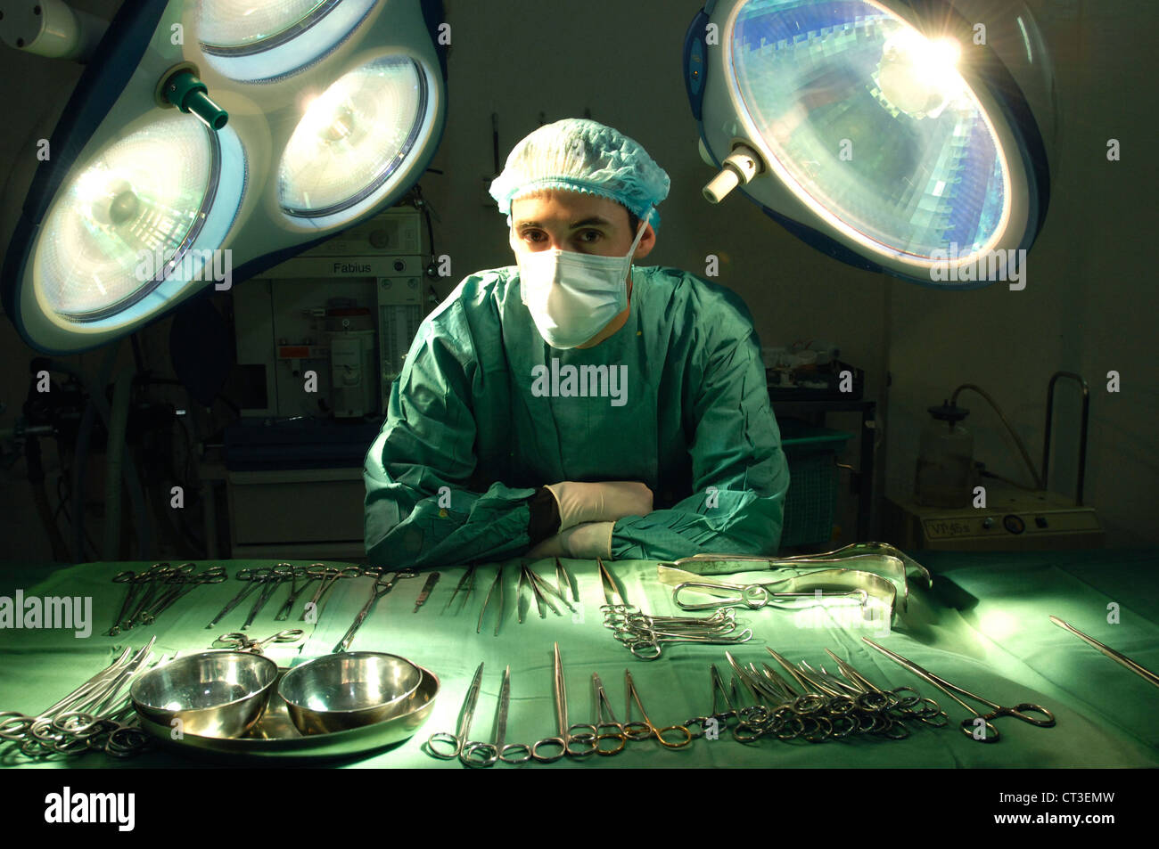 Un chirurgien masqués s'appuyant sur une table d'outils chirurgicaux stériles dans un théâtre de l'hôpital. Banque D'Images