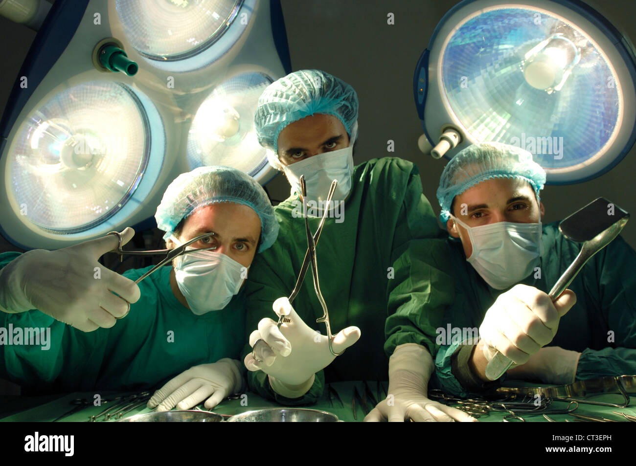 Chirurgiens debout sous les feux d'opération chirurgicale, brandissant divers outils à main. Banque D'Images