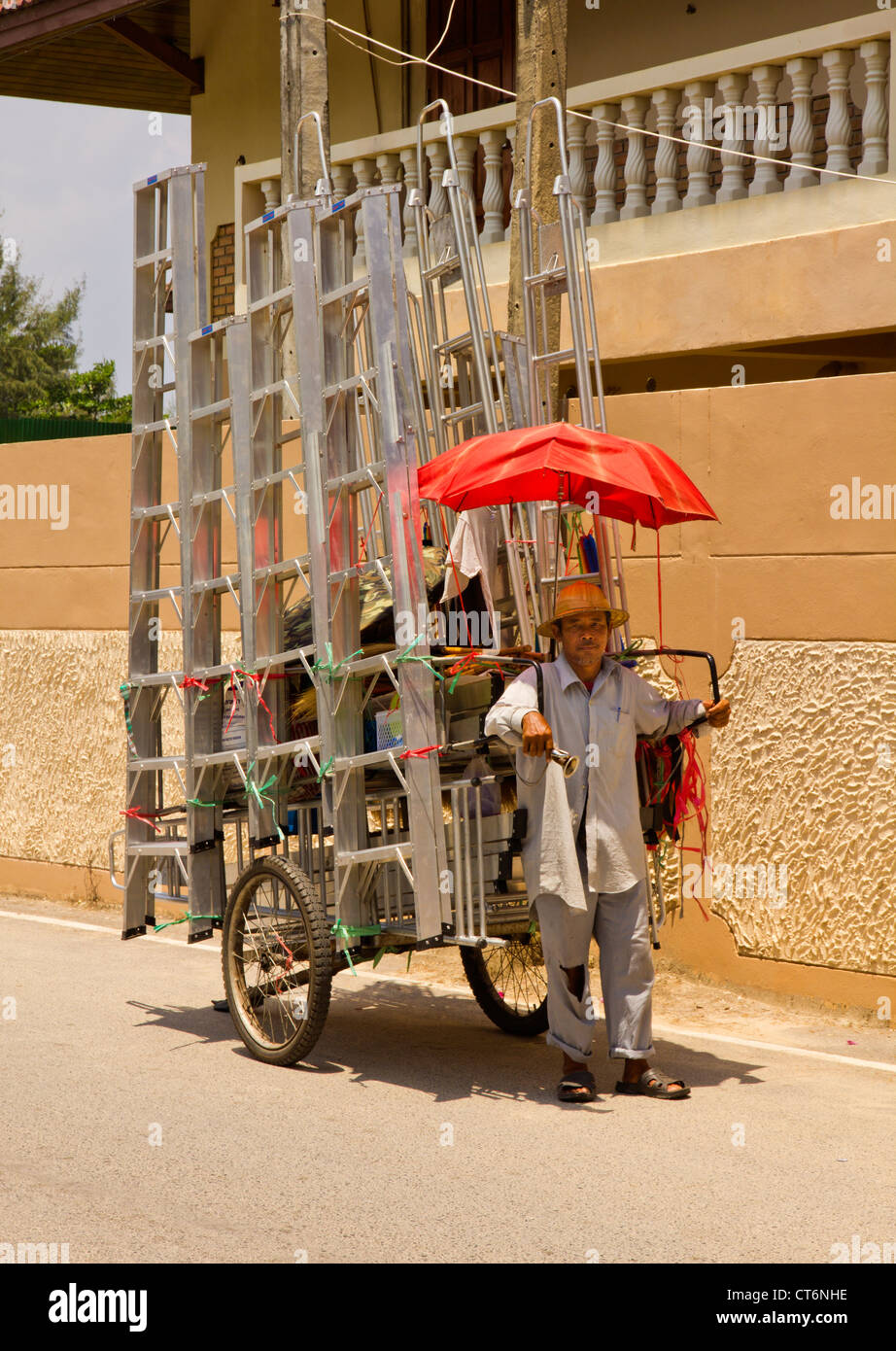 Thai man tirant une charrette chargée de les échelles en aluminium qu'il a à vendre. Banque D'Images